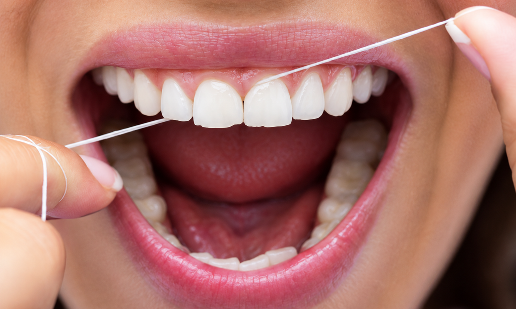 Close-up of a person flossing between healthy teeth and along the gumline