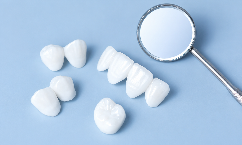 Porcelain dental crowns displayed beside a dental mirror on a blue background.
